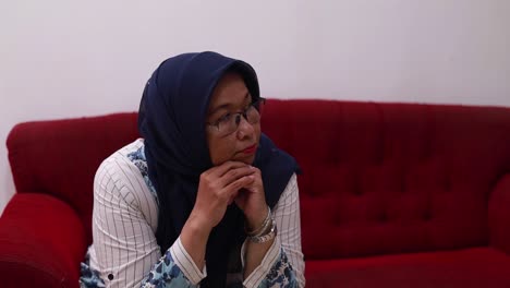 Asian-elderly-woman-sitting-on-the-sofa-at-home-while-looking-sideways