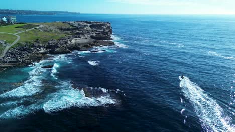 Drone-aerial-of-lifeguard-on-rescue-jet-ski-around-headland-rocky-cliff-landscape-point-watercraft-sports-Maroubra-bay-Sydney-Bondi-Australia