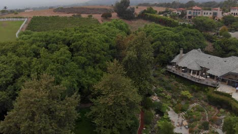 Pulling-back-aerial-shot-of-vineyards,-horse-stables-and-luxury-homes-around-mountain-canyons-near-Malibu,-Ca