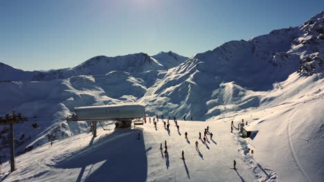 Sunny-day-at-skilift-with-people-in-Austrian-Alps-mountains,-aerial