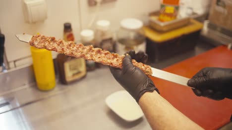 Hand-prepping-spicy-kebab-skewer-in-a-bustling-shop,-warm-indoor-lighting,-culinary-craftsmanship-on-display