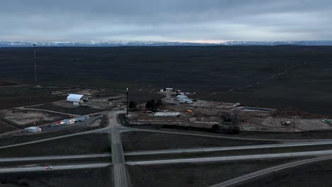 Drone-flying-orbit-around-commercial-building-construction-gas-station-in-barren-desert-winter-landscape-in-the-late-evening