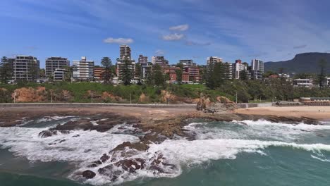 Over-the-surf-and-rocks-towards-people-walking-on-the-beach-path-with-highrise-buildings-beyond