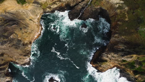 Static-aerial-view-of-Pacific-Ocean-waves-crashing-against-rocky-cove,-Oregon-coast