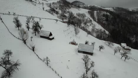 Montañas-Nevadas-Con-Cabañas-Aisladas,-árboles-Sin-Hojas-Y-Senderos-Sinuosos,-Vista-Aérea