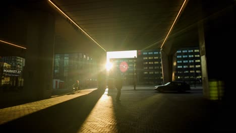 Man-walking-under-urban-overpass-with-low-warm-sun-as-backlight-in-modern-suburb