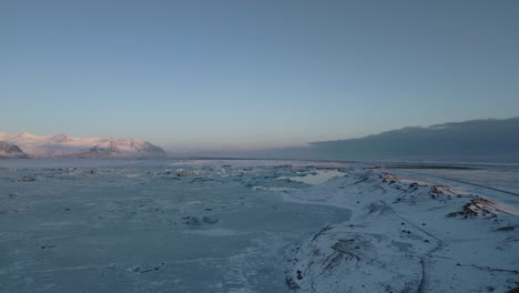 Flying-above-frozen-empty-land,-snowy-countryside-during-sunset,-South-Iceland