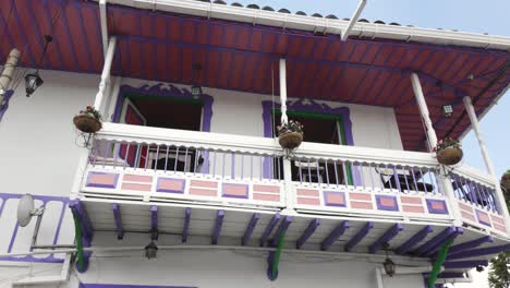 Panorámica-De-ángulo-Bajo-De-Una-Hermosa-Casa-Colombiana-Con-Un-Colorido-Balcón-En-Colores-Rosa-Y-Lavanda-Y-Plantas-En-Macetas.