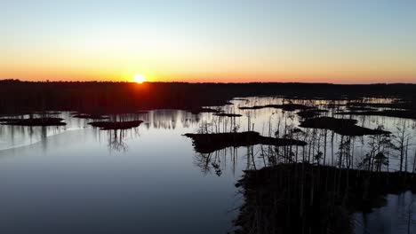 Una-Hermosa-Puesta-De-Sol-Sobre-Un-Lago-Con-Algunos-árboles-Al-Fondo