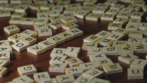 Person-playing-with-Scrabble-tile-letters-on-table-spells-word-VEGAN