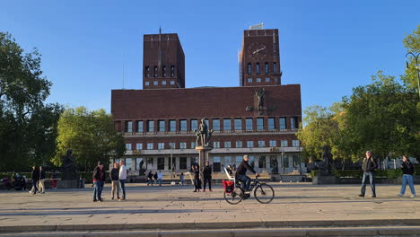 Ayuntamiento-De-Oslo,-Noruega,-Vista-Desde-El-Paseo-Marítimo-Junto-Al-Fiordo,-Gente-Y-Edificio-Bajo-La-Luz-Del-Sol-De-La-Hora-Dorada