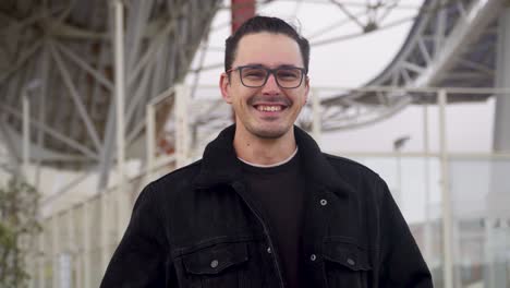 Portrait-of-a-cheerful,-smiling-young-man-wearing-a-black-jacket-and-glasses
