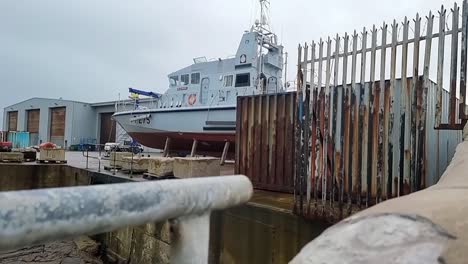 Holyhead-marine-services-patrol-boat-reveal-behind-secured-industrial-fence-in-maritime-dockyard