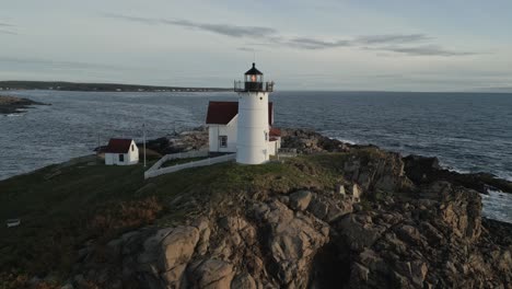 Aerial-view-of-rocky-island-with-a-beautiful-white-lighthouse-on-top,-during-sunset