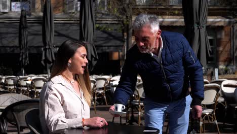 Un-Camarero-Canoso-Trae-Un-Café-En-Una-Terraza-En-El-Sur-De-Francia-A-Una-Bella-Joven-Sentada