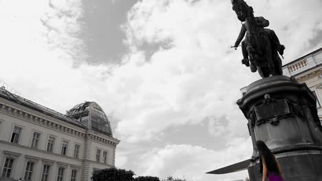 Girl-walks-past-statue-in-black-and-white,-Vienna,-dark-mood,-cloudscape