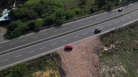 a-dramatic-aerial-footage-of-a-red-car-travelling-alongside-the-sea-on-a-highway