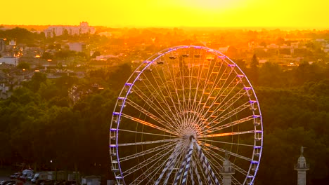 Ferris-Wheel-in-Place-des-Quinconces-Bordeaux-France,-rotating-and-flickering-at-sunset,-Aerial-tilt-up-shot