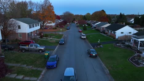 American-neighborhood-at-dusk-with-car-driving-towards-drone,-reverse-dolly