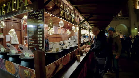 Gente-Tomando-Su-Pedido-En-Puestos-Navideños-Con-Comida-Por-La-Noche-En-La-Plaza-Principal-Del-Mercado-De-Cracovia,-Polonia.