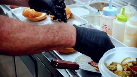 Imágenes-Cinematográficas-De-Cocina-De-Comida-De-4k-De-Un-Chef-Preparando-Y-Haciendo-Una-Deliciosa-Hamburguesa-Casera-En-La-Cocina-De-Un-Restaurante-En-Cámara-Lenta-Colocando-El-Tocino-Encima-De-La-Hamburguesa-Con-Queso