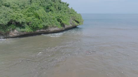 Low-altitude-aerial-drone-shot-over-polluted-muddy-sewage-water-and-floating-trash-with-debris-over-dead-coral-reef-mixing-with-turquoise-water-and-tropical-coastine-in-Bali-Indonesia