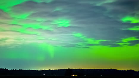 Northern-lights-aurora-borealis-glowing-green-over-a-forest-landscape-illuminating-the-clouds---time-lapse