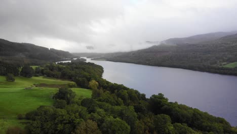 Vista-Aérea-Sobre-Los-árboles-De-La-Orilla-Del-Río-Green-Valley-Con-El-Lago-Tummel-En-El-Fondo