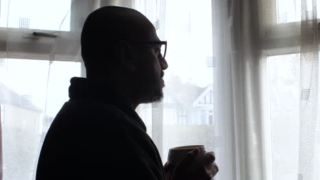 Silhouette-Eines-Mannes,-Der-Am-Fenster-Kaffee-Schlürft-Und-In-Einem-Moment-Der-Einsamkeit-Das-Morgenlicht-Reflektiert