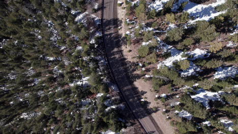 Top-down-view-of-a-snowy-mountain-road-turning-through-the-forest-surrounded-by-pine-trees,-drone-shot