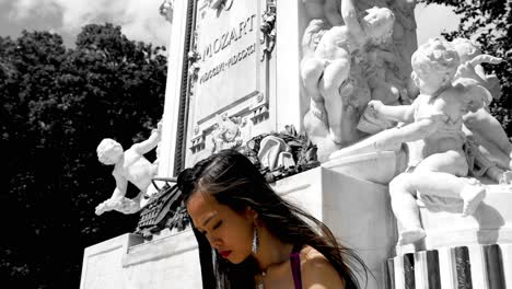 Young-girl-looking-down,-writing,-in-front-of-Mozart-monument-in-Vienna,-Austria,-black-and-white-with-angels