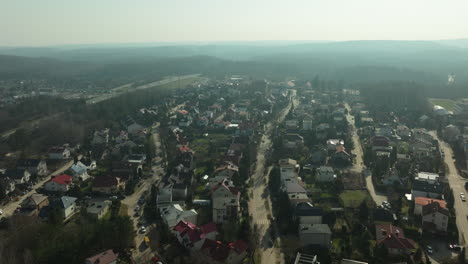 aerial-view-stretches-over-a-residential-street-in-a-suburban-area-of-Gdynia,-showcasing-neat-homes-with-gardens,-intersected-by-roads-and-surrounded-by-the-bare-branches-of-trees-in-winter