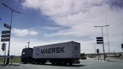 LKWs-Am-Kreisverkehr-Mit-Klarem-Himmel,-Windräder-Im-Hintergrund,-Industrielle-Umgebung