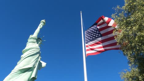 Statue-of-Liberty-Replica-and-American-Flag,-Slow-Motion-Low-Angle