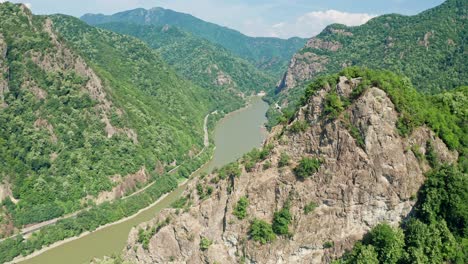 Lush-Cozia-Mountains-with-the-Olt-River-winding-through,-Pietrele-Rosiei-Peak-visible,-sunny-day,-aerial-view