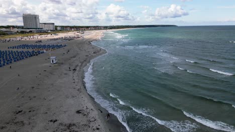 beautiful-beach-at-the-baltic-sea,-people-walk-along-the-beach,-waves-hit-the-coast,-warnemünde,-drone