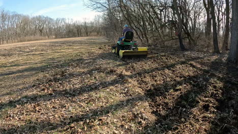 POV-following-a-man-on-utility-tractor-towing-a-rototiller-to-loosen-soil-in-a-wildlife-food-plot-between-timber-and-field-in-early-spring