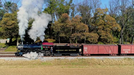 Una-Vista-Aérea-De-Un-Antiguo-Tren-De-Pasajeros-De-Carga-A-Vapor-Que-Echa-Humo-Mientras-Se-Pone-En-Marcha-Lentamente-En-Un-Día-De-Otoño