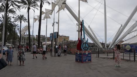 Groups-of-people-walking-through-paved-area-next-to-Genoa-port,-on-a-grey-cloudy-day