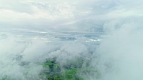 Flying-through-clouds-with-green-landscape-bellow,-aerial-view