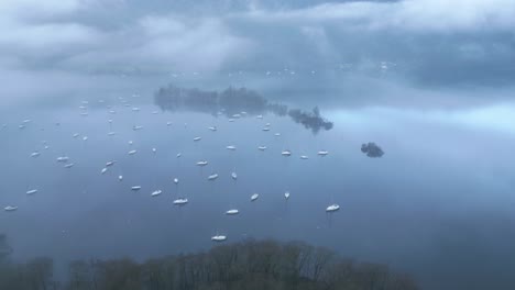 Retreating-drone-shot-of-the-Windermere-Lake,-showing-the-sailboats-sailing-and-floating-in-the-waters-of-the-Lake-District-of-Cumbria-in-England