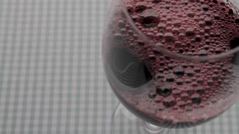Pouring-red-wine-into-glass,-close-up-on-gingham-cloth-background,-focus-on-flow-and-texture