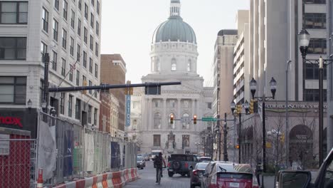 View-down-the-road-in-Indianapolis,-Indiana-of-the-Indiana-state-capitol-building-with-vehicle-traffic-and-a-bicyclist-riding-by-with-stable-video