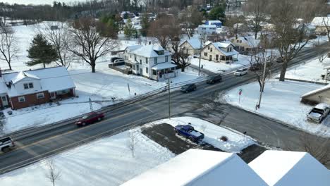 Line-of-cars-slowly-drive-through-American-town-covered-in-winter-snow