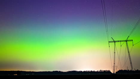 Cielo-Estrellado-Girando-Y-El-Tiempo-De-Las-Nubes-Pasa-Sobre-Los-Postes-De-Transmisión-De-Energía-Con-El-Horizonte-De-La-Aurora-Boreal