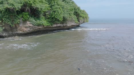 Low-altitude-aerial-drone-shot-over-polluted-muddy-sewage-water-and-floating-trash-with-debris-over-dead-coral-reef-mixing-with-turquoise-water-and-tropical-coastine-in-Bali-Indonesia