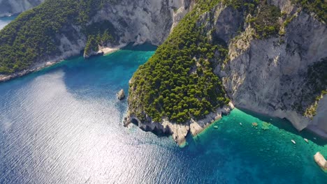 Orbiting-drone-shot-of-the-rocky-coastline-of-Oasi-beach,-as-a-boat-passes-by-the-cove-near-the-village-of-Chania,-in-the-island-of-Crete-in-Greece