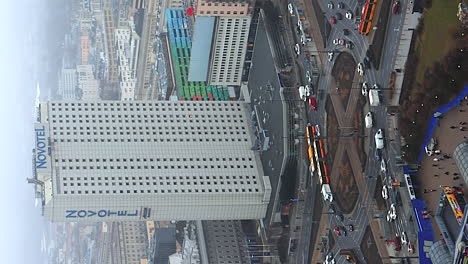 Traffic-driving-through-traffic-circle-outside-Novotel-building-Warsaw,-vertical