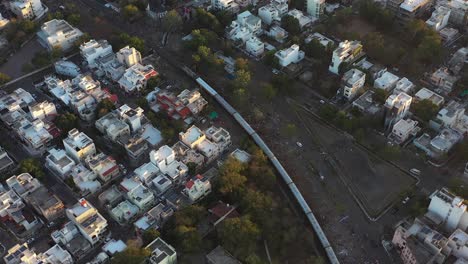 Vista-Aérea-De-Drones,-Un-Gran-Tren-Se-Mueve-Desde-Atrás-Y-Muchos-Edificios-Residenciales-Son-Visibles-Alrededor