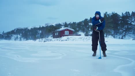 The-Man-is-Employing-a-Hand-operated-Auger-to-Bore-Hole-in-the-Frozen-Lake-for-Ice-Fishing-in-Bessaker,-Trondelag-County,-Norway---Static-Shot